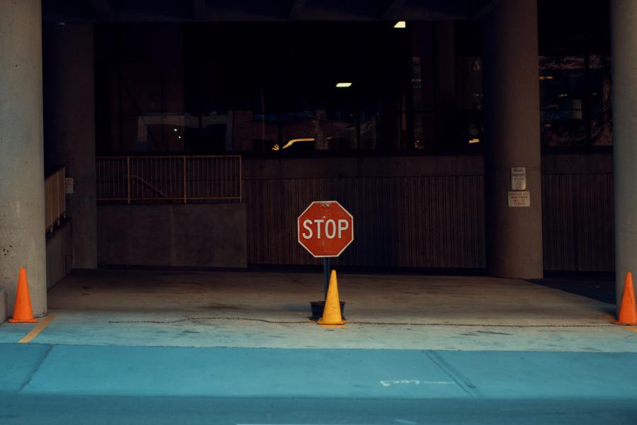 An exterior shot of the entry to a garage, warehouse or workshop. Three traffic cones stand in a row on the perimeter and a stop sign is positioned in the centre.