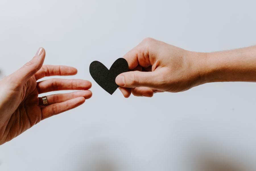 Hands of two people holding either side of paper heart. One person letting go.