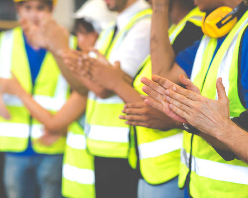 Workers in high-vis vests standing in a group discussing and clapping.