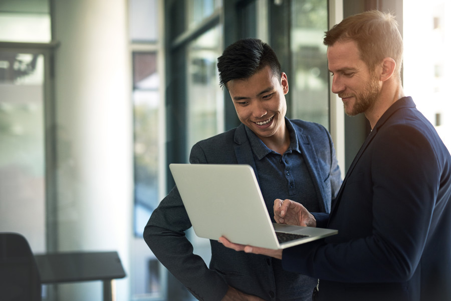 Two professionals standing together working on a laptop.