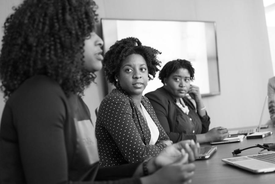 Three women sitting at a table during a meeting. The woman closest to the camera is speaking while the other two are turned toward her listening. 