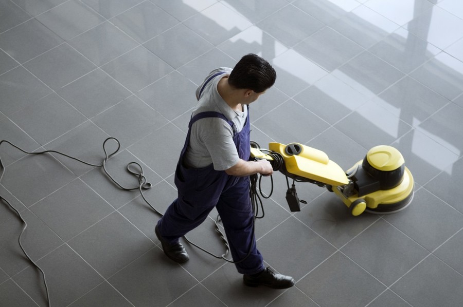 Cleaner cleaning a tiled floor in a building foyer.
