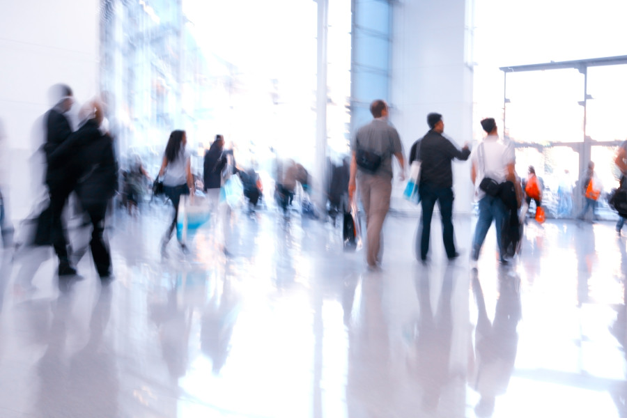 Blurry establishing shot of a number of consumers or commuters walking through a large white space.