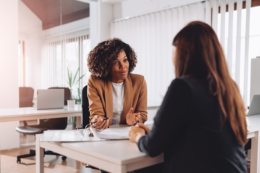 Two workers sitting at opposite ends of a table or desk, talking