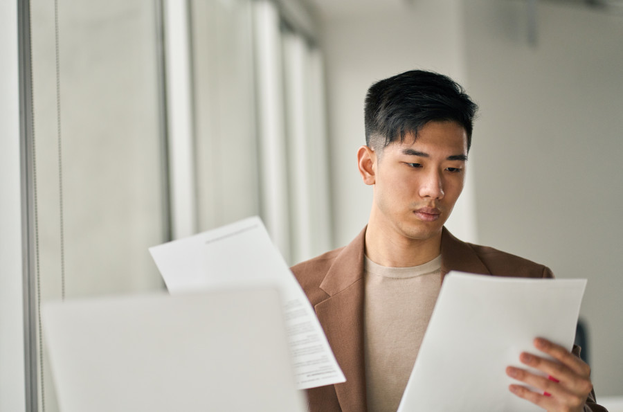 Man sitting at a computer examining two documents he has just received by mail. 