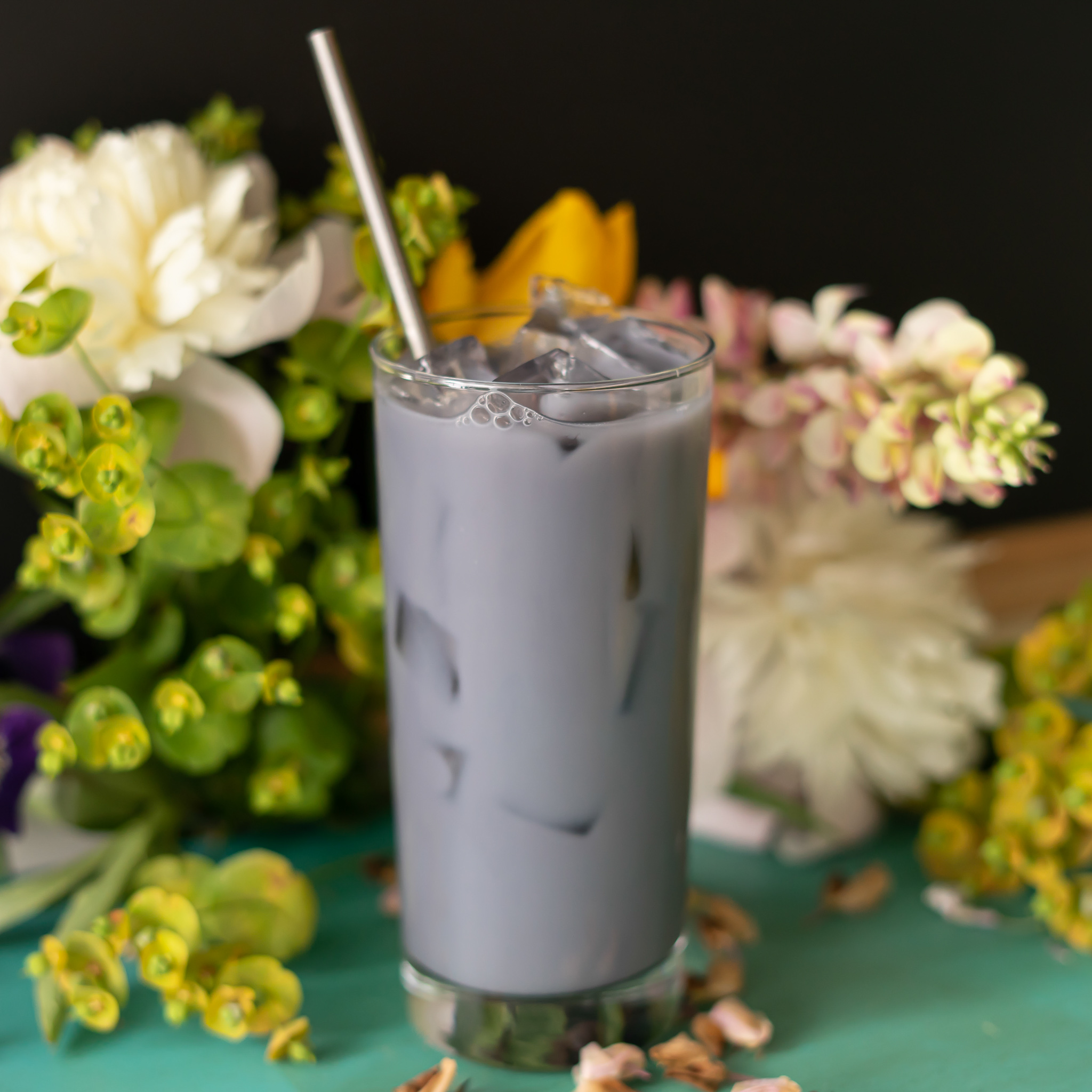 A lavender colored iced tea drink in a tall, slim glass against a floral background