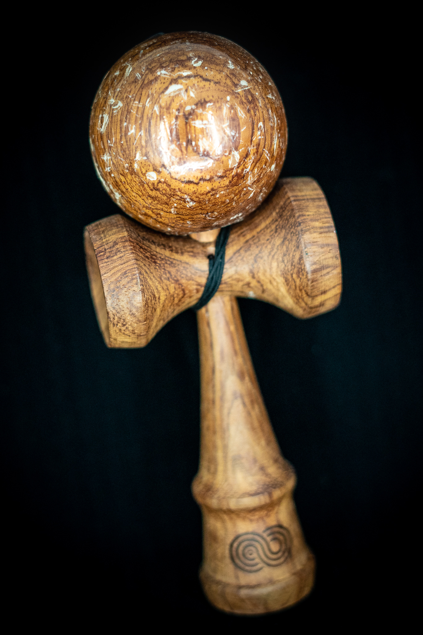 Kendama on black background. A wood toy consisting of a handle, two cups, a spike, and a ball attached to a string. Made of dark mahogany 