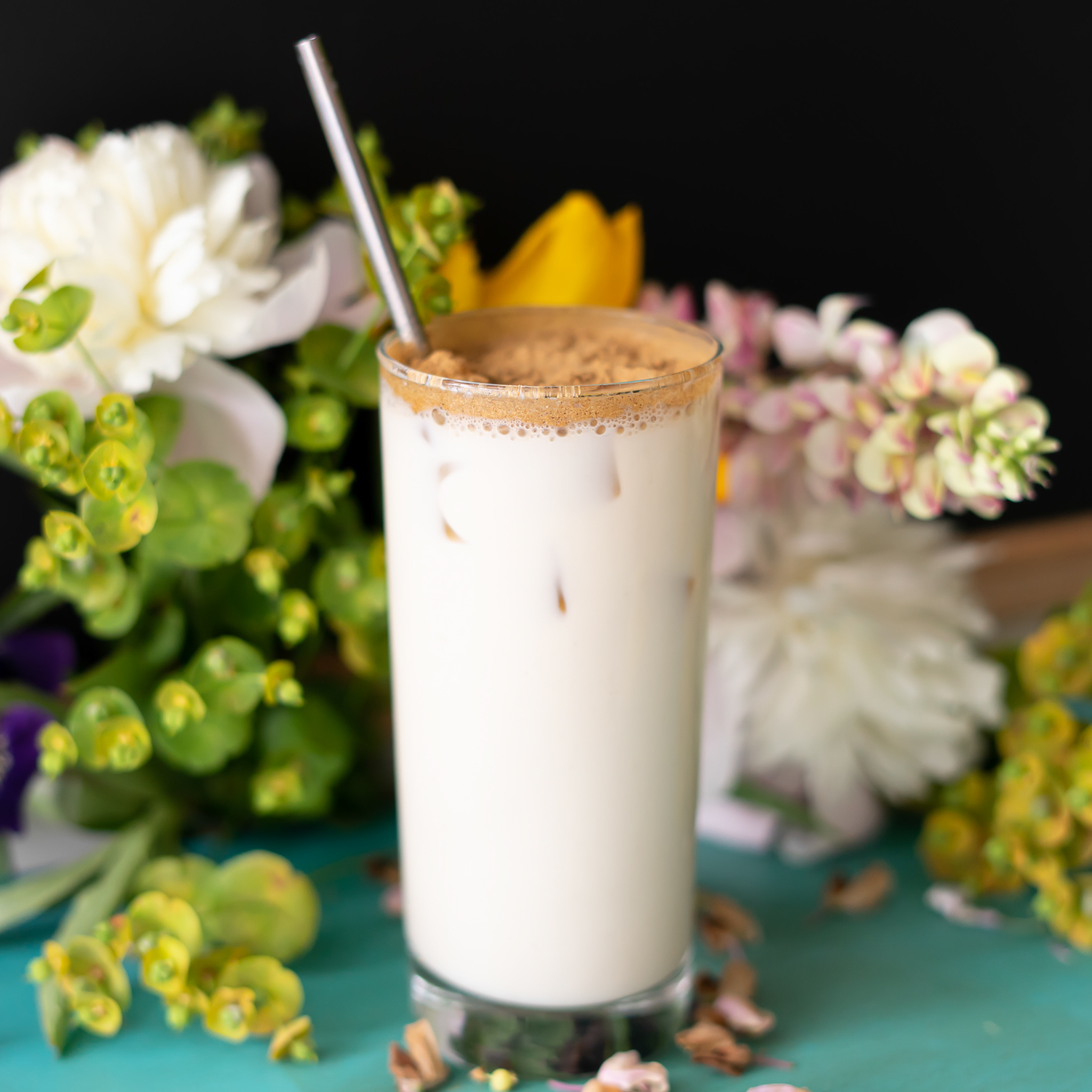 A milky white iced tea late in a tall slim glass sits against a floral background.