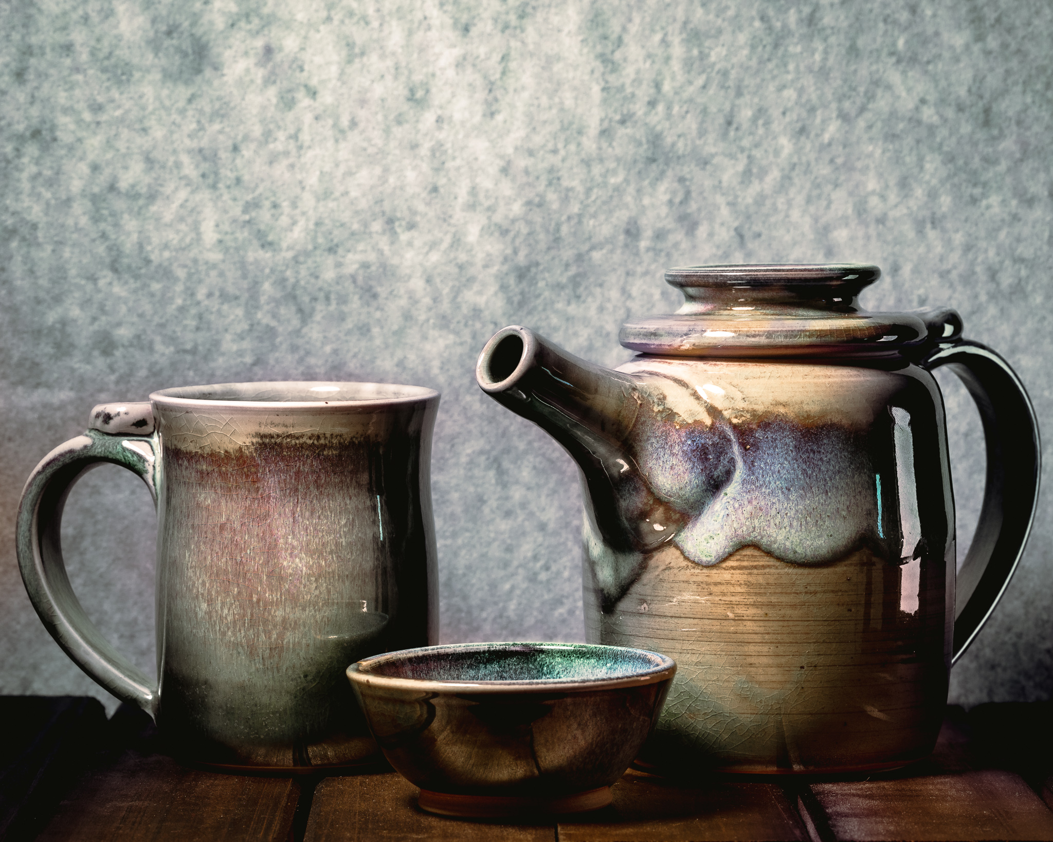 A teaset of handmade ceramic goods, consisting of a mug, and dish, and a teapot.