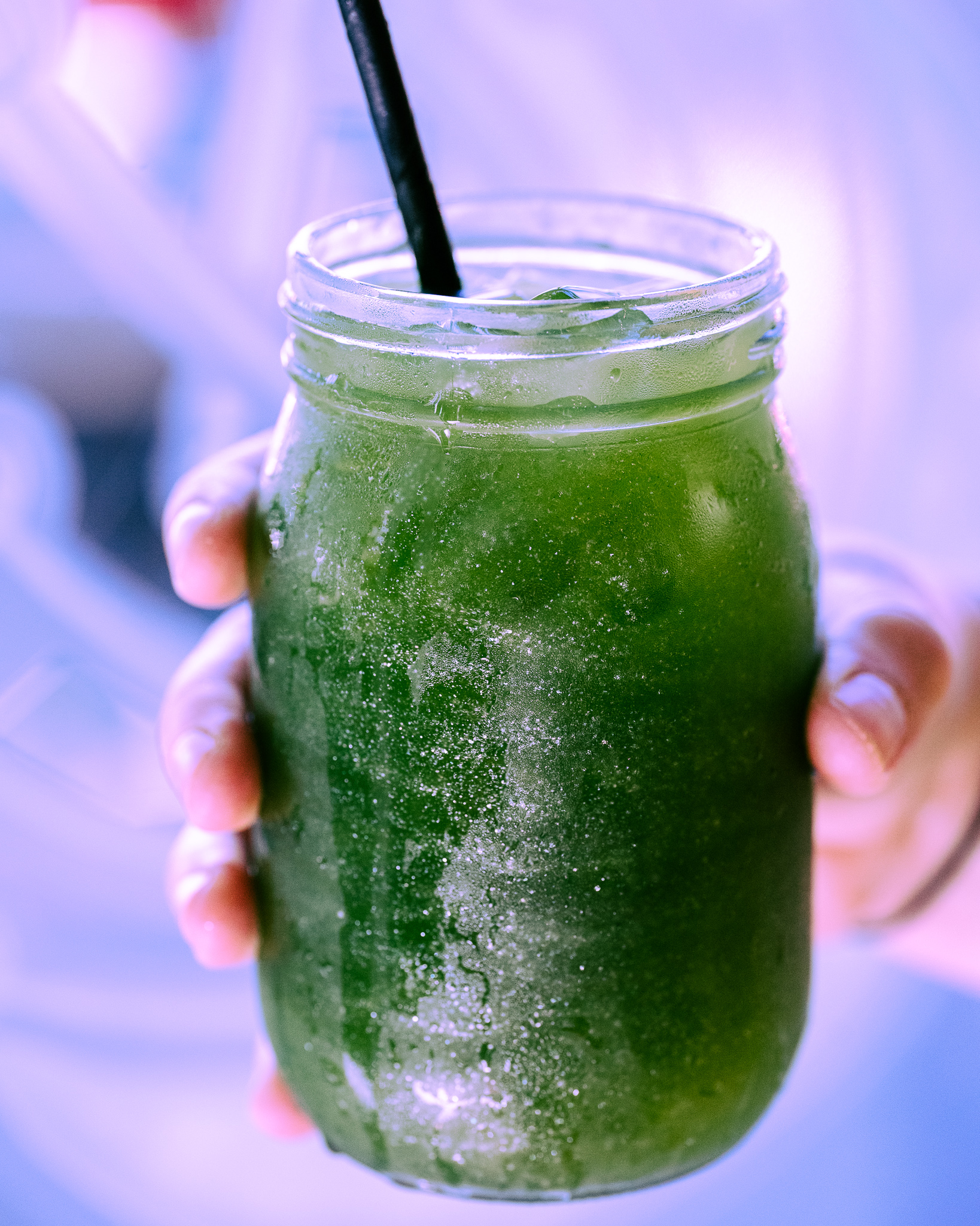 close up of a hand holding a glass jar containing a bright green iced tea drink with shiny edible glitter