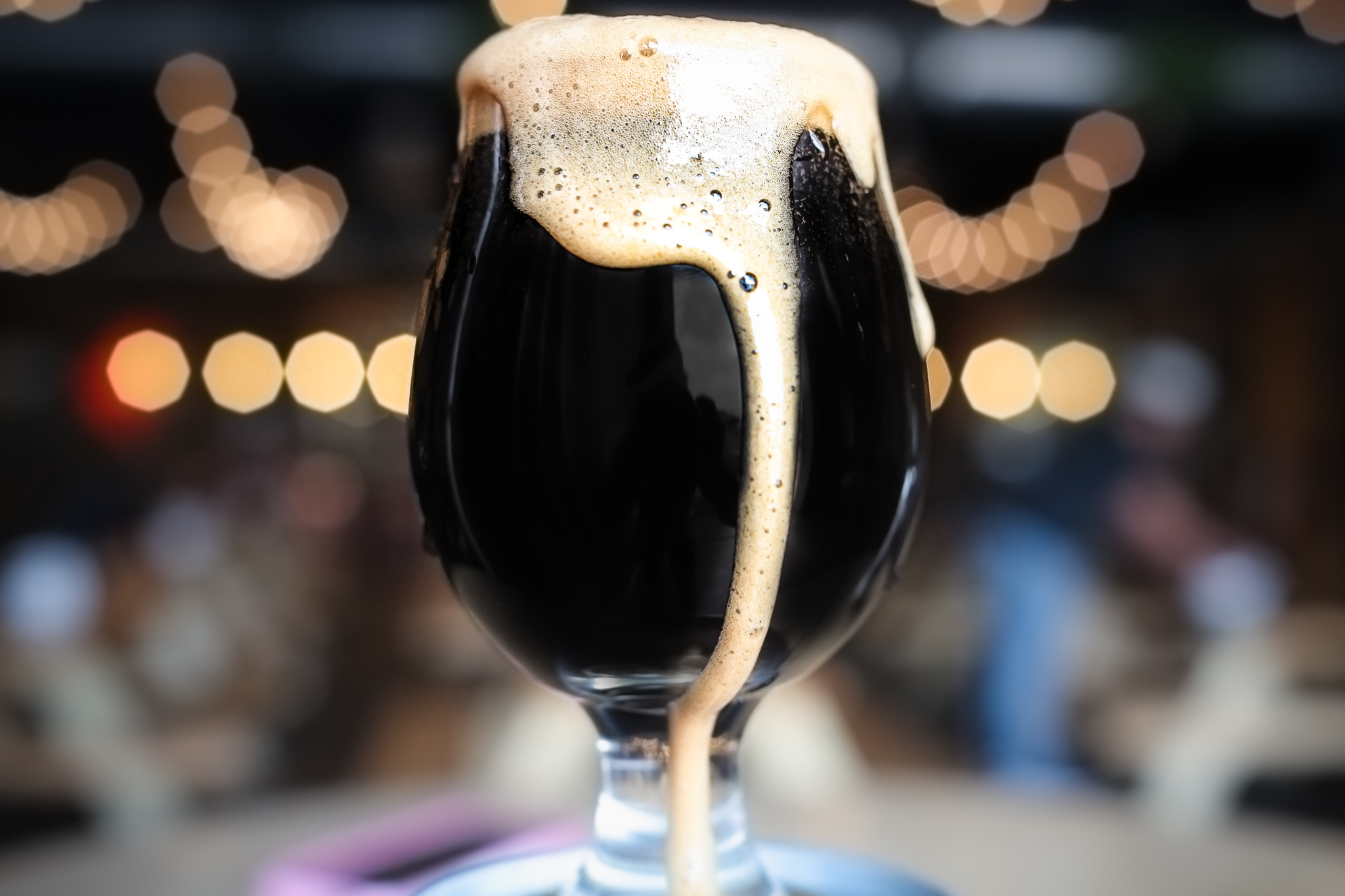 A dark imperial stout overflows out of a tulip shaped beer glass
