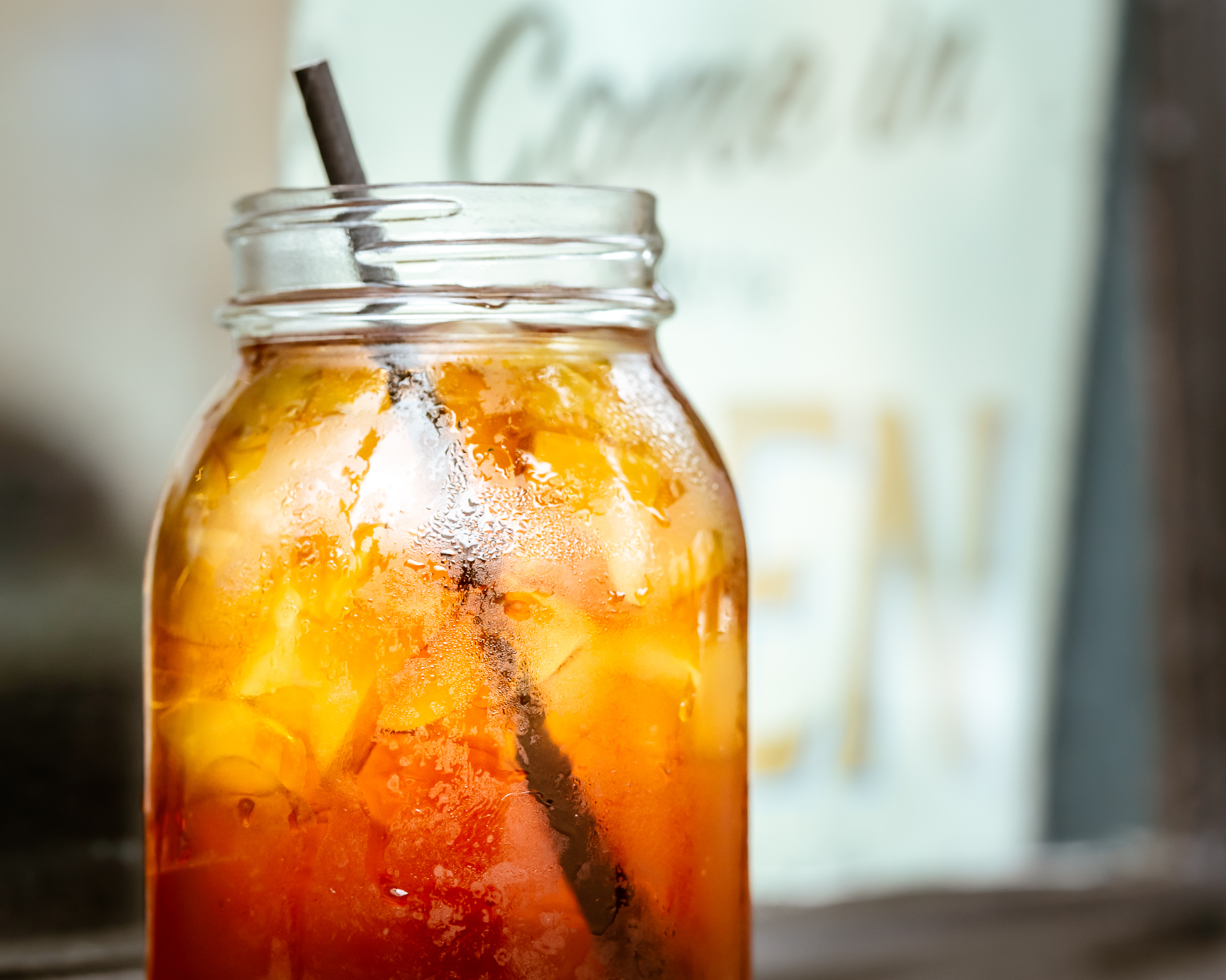A jar of iced tea with a straw in it in front of a "come on in, we're open" sign