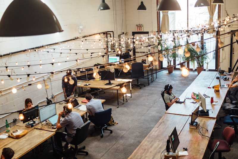a photo a busy co-working area. three rows of desks with people sitting at computers working
