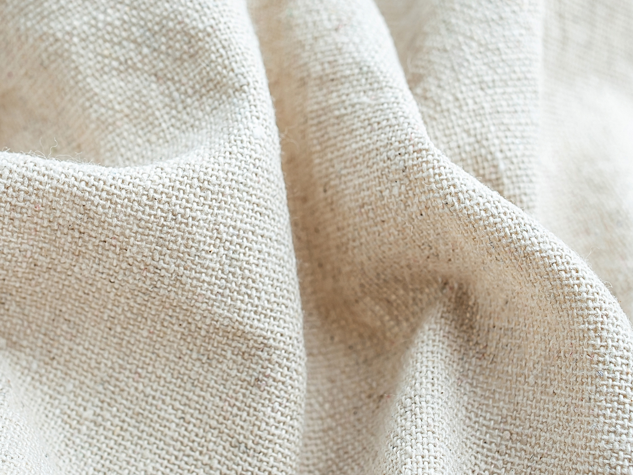 Beiges Leinenstoffgewebe mit sichtbarer Struktur und Falten.