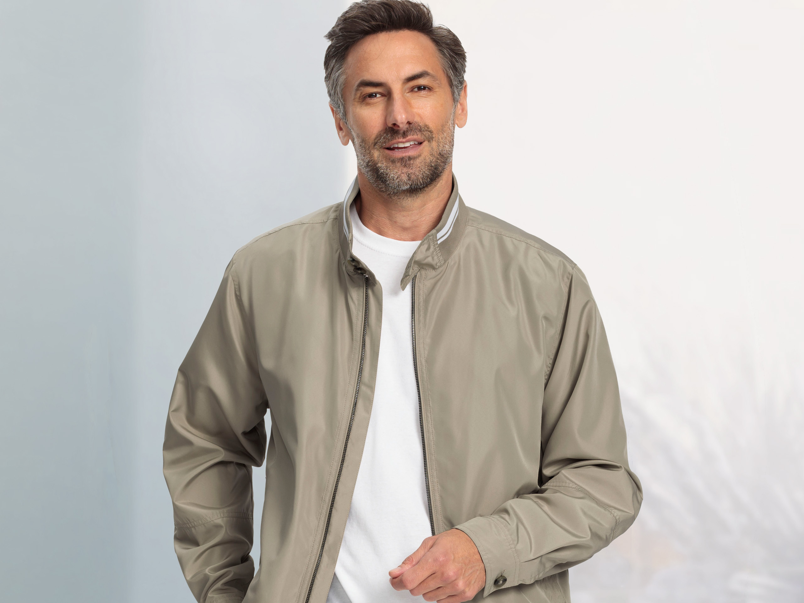 Mann mit beiger Jacke und weißem Shirt vor hellem Hintergrund.