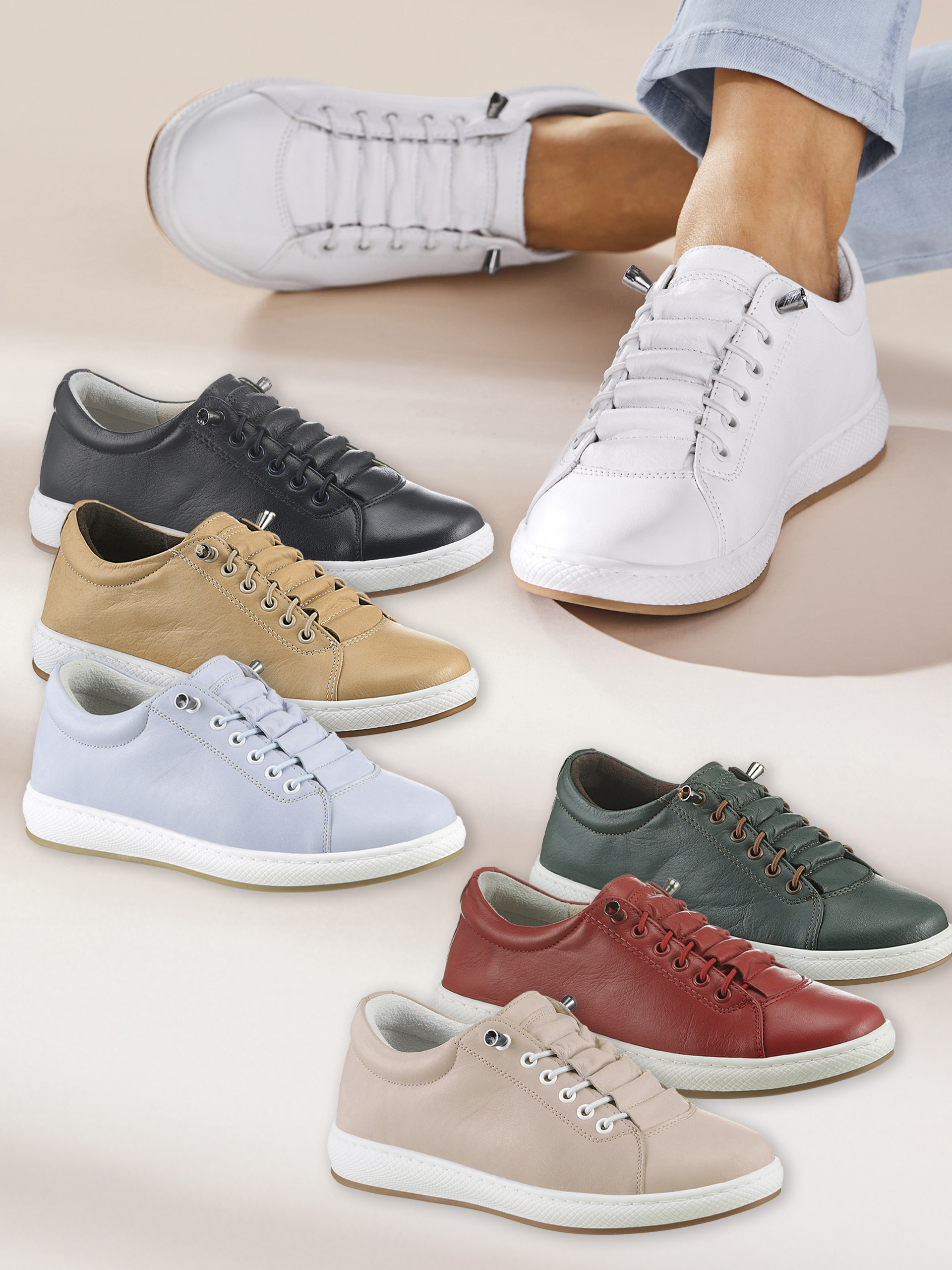 Verschiedene Paar Sneaker aus Leder in sechs Farben liegen nebeneinander, ein Fuß trägt weiße Sneaker.