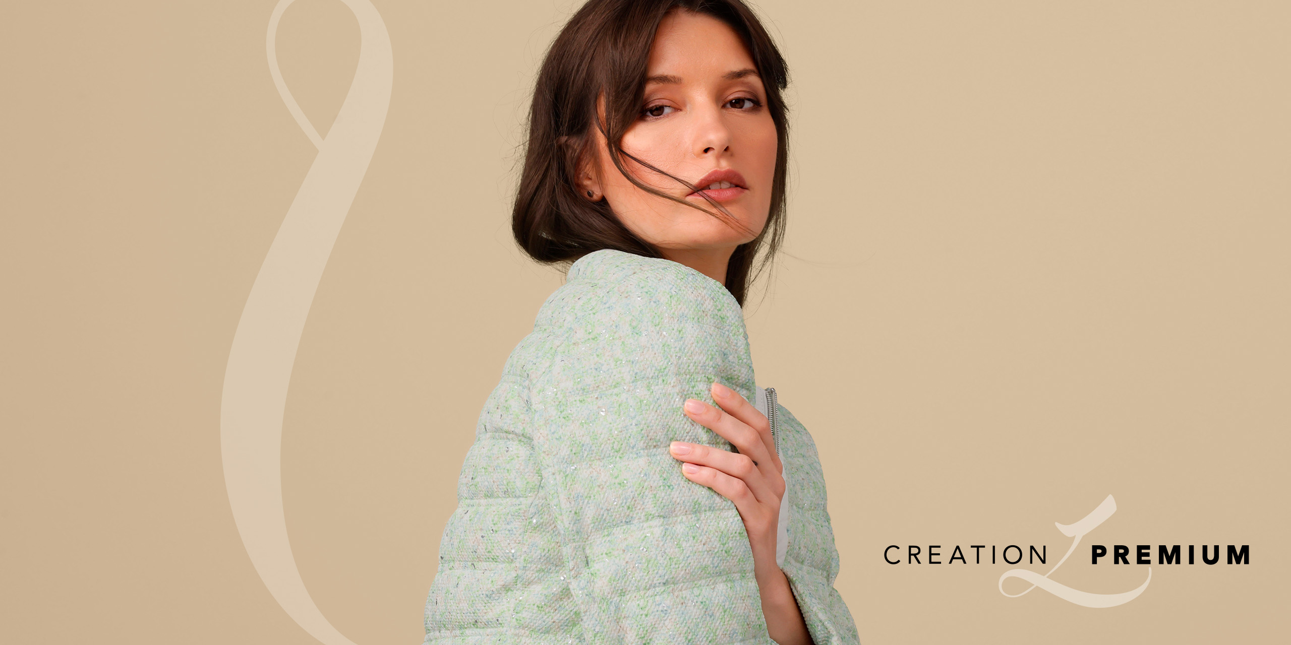 Ein Model sitzt auf einem Stuhl, trägt einen gemusterten Blazer in Blau- und Grüntönen zu weißer Hose. Text: CREATION PREMIUM.