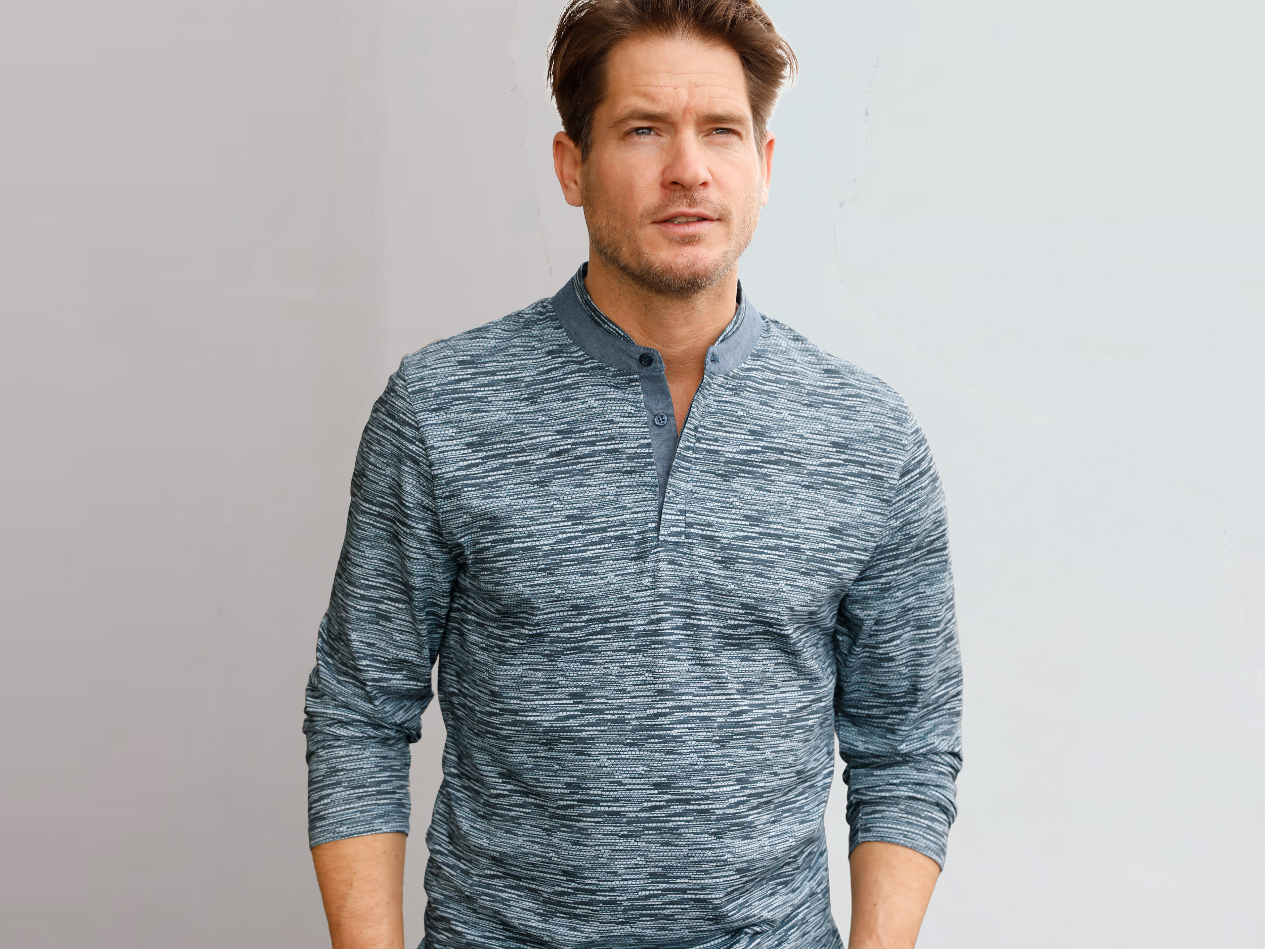 Mann mit blau gemustertem Langarmshirt vor hellem Hintergrund.