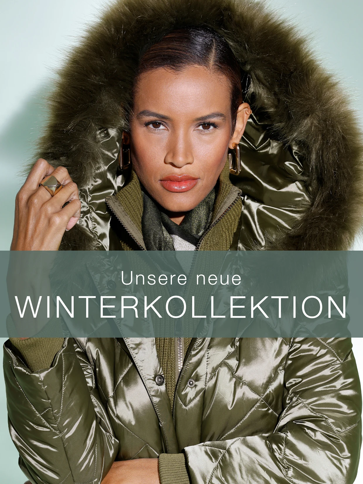 Ein Model trägt eine glänzende Winterjacke mit Fellkapuze in grün. Text: 'Unsere neue WINTERKOLLEKTION'.