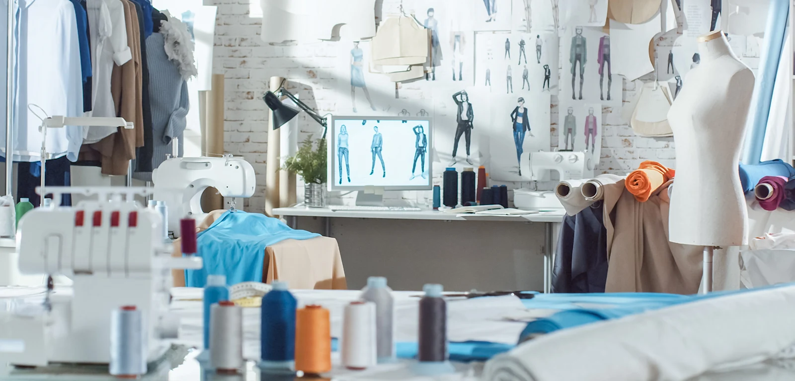 Nähatelier mit Stoffrollen, Garnspulen, Schneiderpuppe, Nähmaschinen und Skizzen von Kleidungsdesigns an der Wand. Nähatelier mit Stoffrollen, Garnspulen, Schneiderpuppe, Nähmaschinen und Skizzen von Kleidungsdesigns an der Wand.