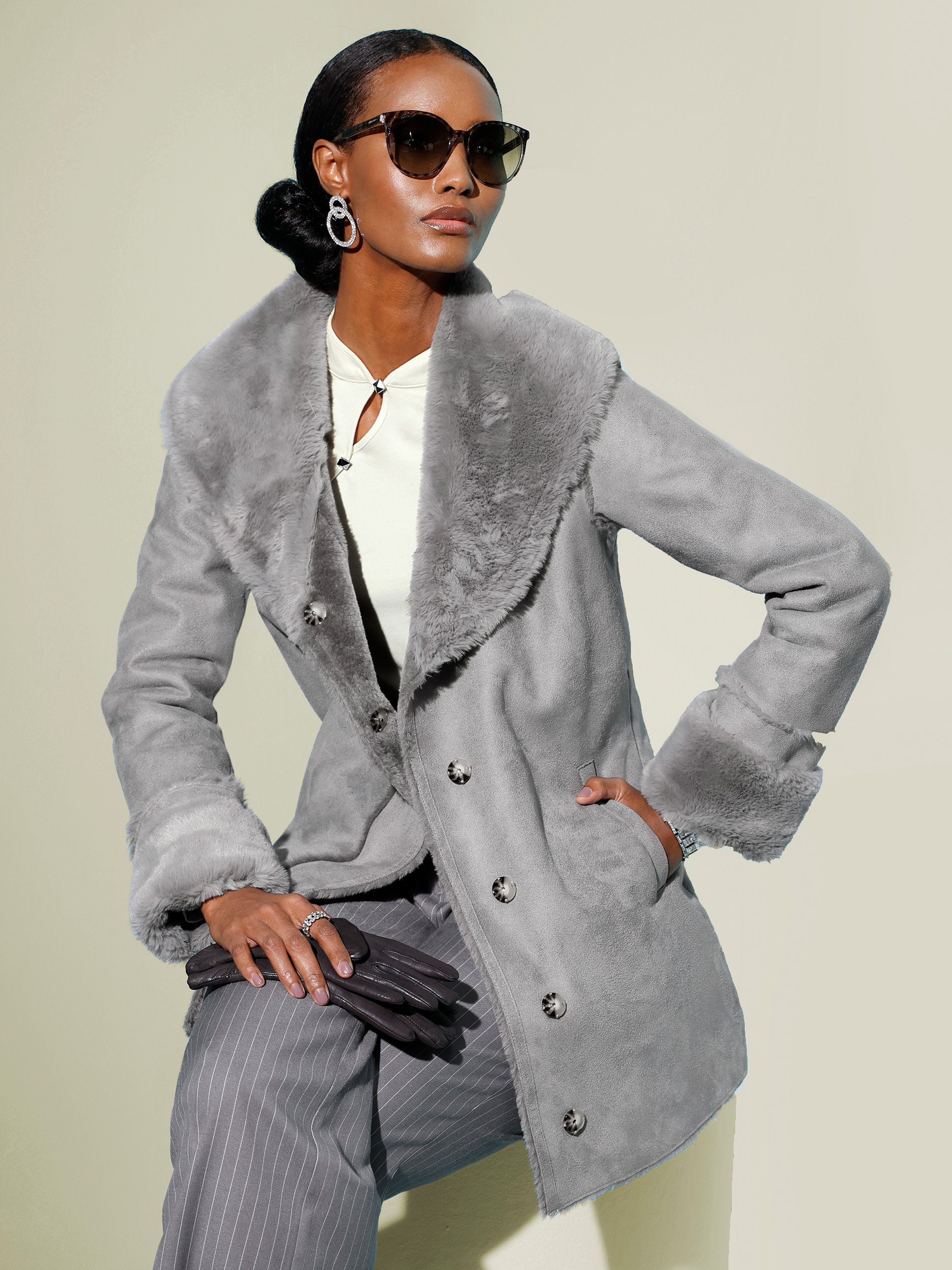 Model mit grauem Mantel und Sonnenbrille steht vor pastellgrünem Hintergrund.