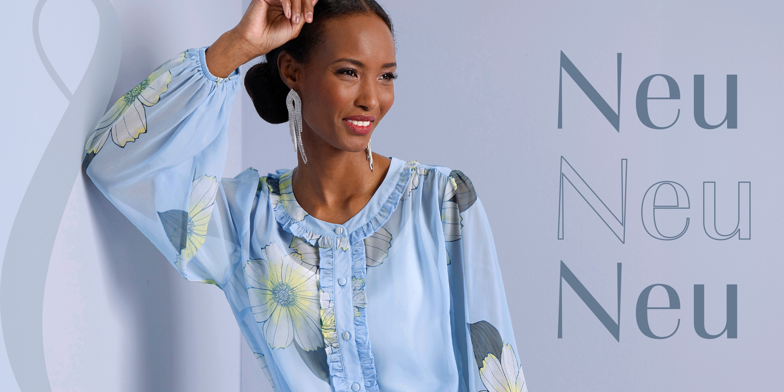 Ein Model trägt eine hellblaue Bluse mit großem Blumenmuster und Rüschenkragen, dazu auffällige Ohrringe. Links steht mehrfach 'Neu'.
