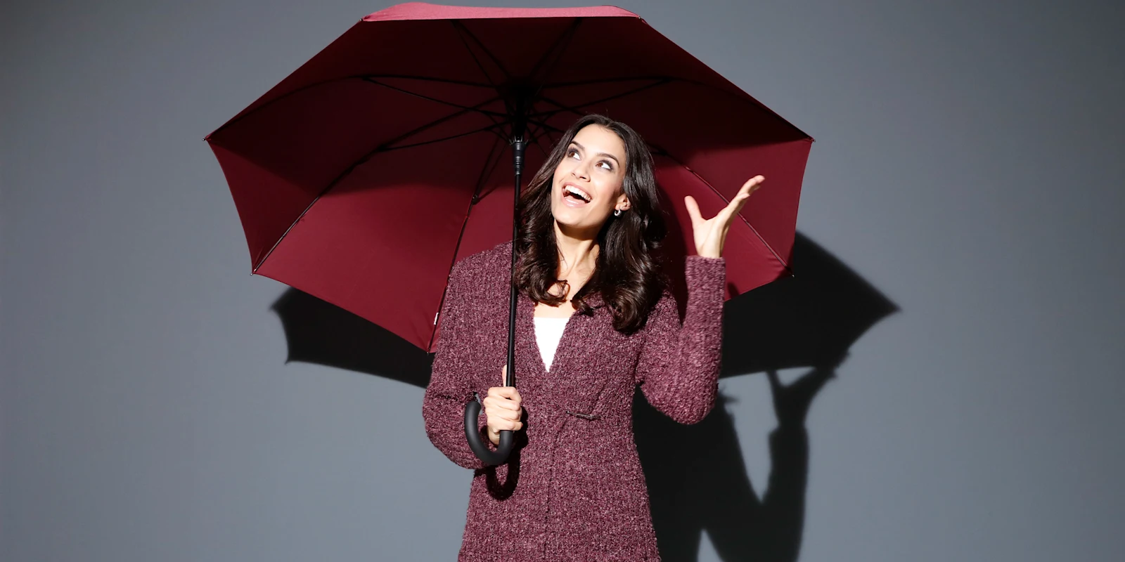 Ein Model hält einen roten Regenschirm und gestikuliert mit der anderen Hand vor einem grauen Hintergrund. Ein Model hält einen roten Regenschirm und gestikuliert mit der anderen Hand vor einem grauen Hintergrund.