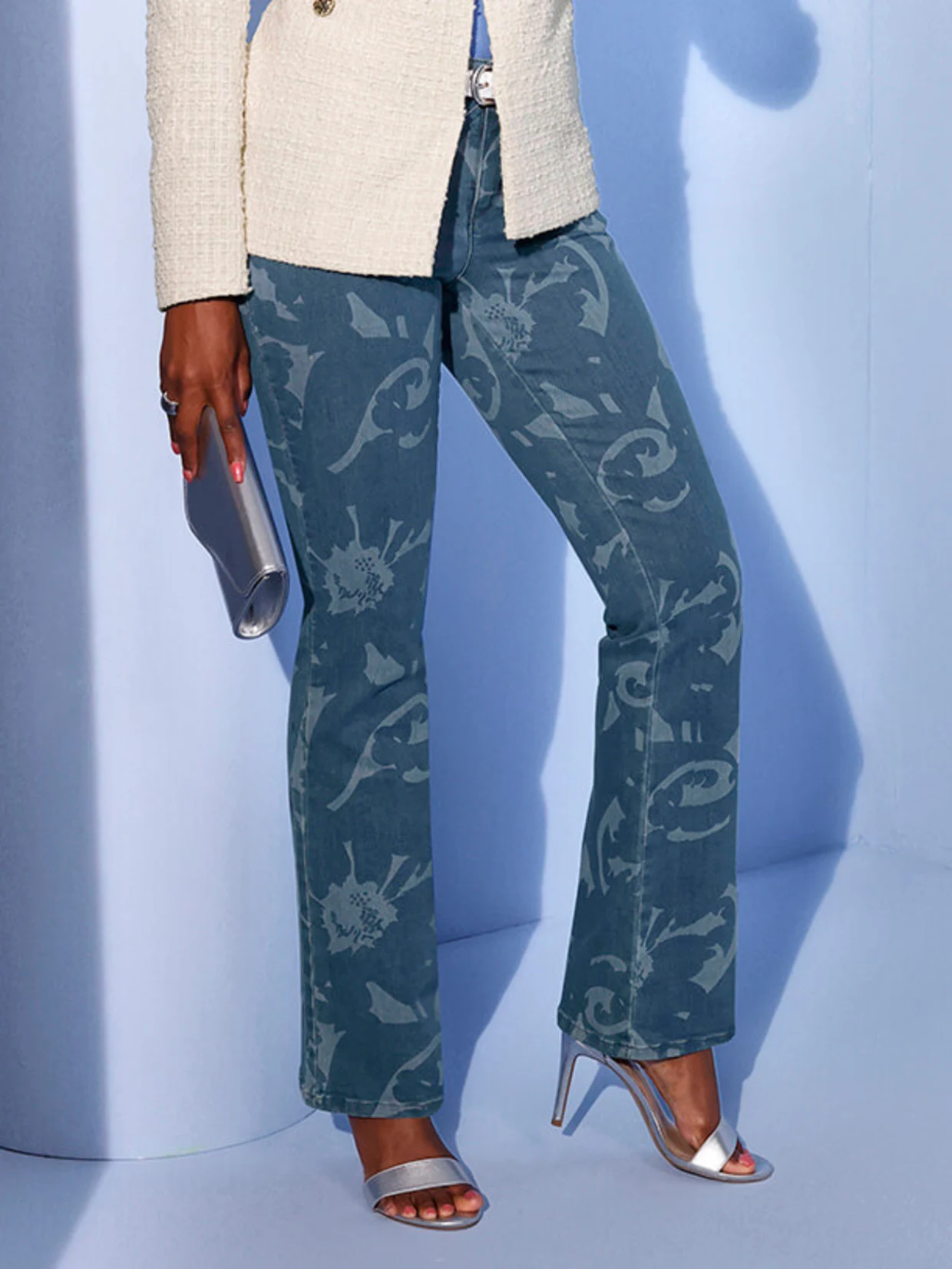 Ein Model trägt eine helle Jacke und gemusterte Jeans vor einem blauen Hintergrund.