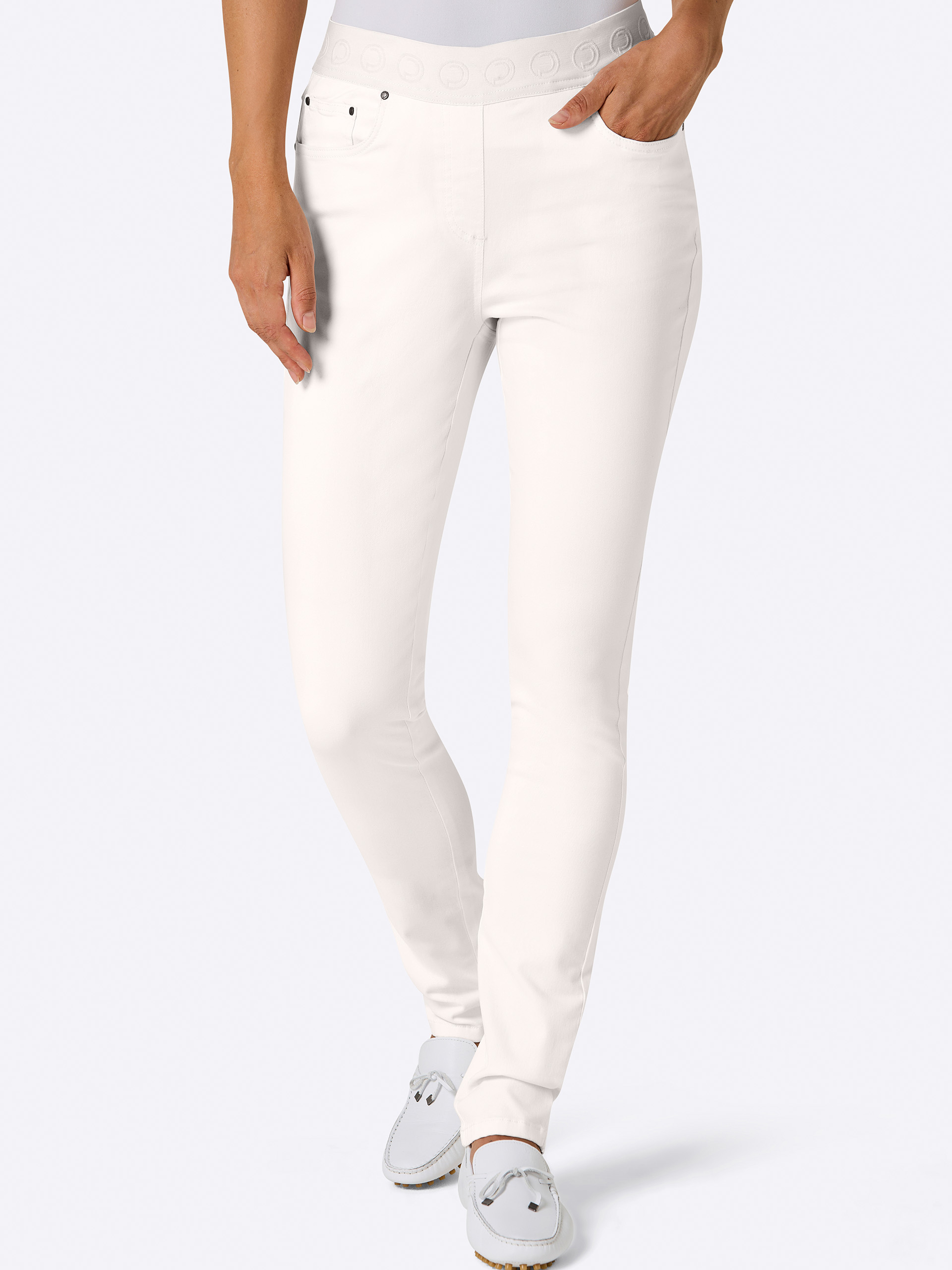 Ein Model trägt eine weiße, schmal geschnittene Hose mit elastischem Bund und weiße Mokassins. Der Hintergrund ist hell.