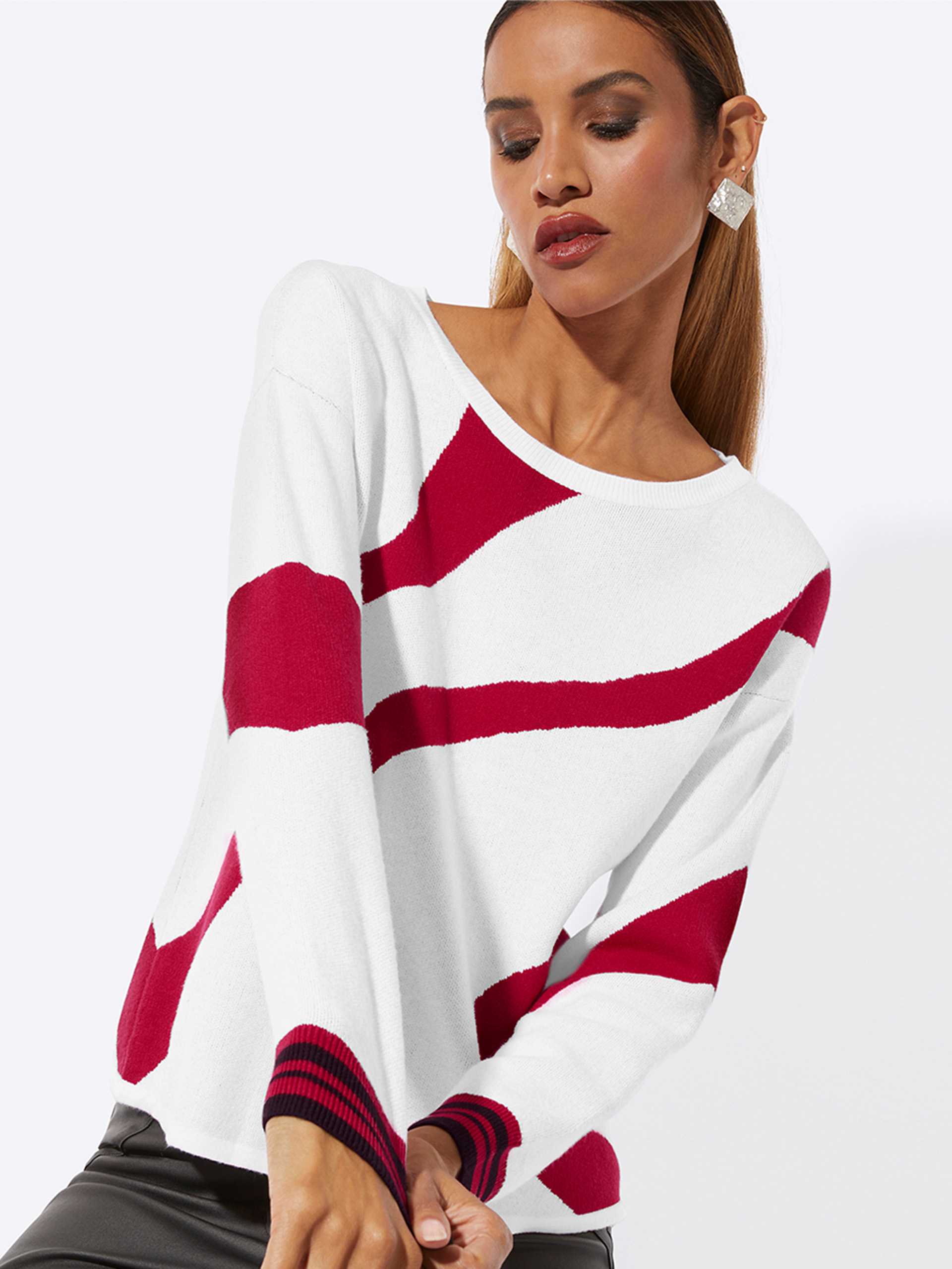 Das Bild zeigt eine Frau in einem weiß-roten Pullover mit auffälligen, geschwungenen Streifen. Der Pullover hat breite Bündchen an den Ärmeln. Die Darstellung ist zweigeteilt, wobei die rechte Seite einen etwas näheren Ausschnitt zeigt.