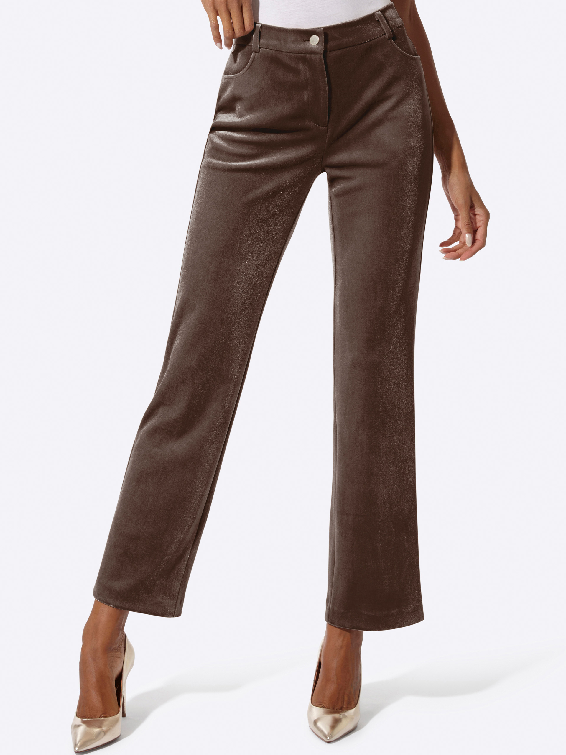 Ein Model trägt eine braune, gerade geschnittene Hose aus samtigem Stoff und beigefarbene High Heels. Der Hintergrund ist hell.