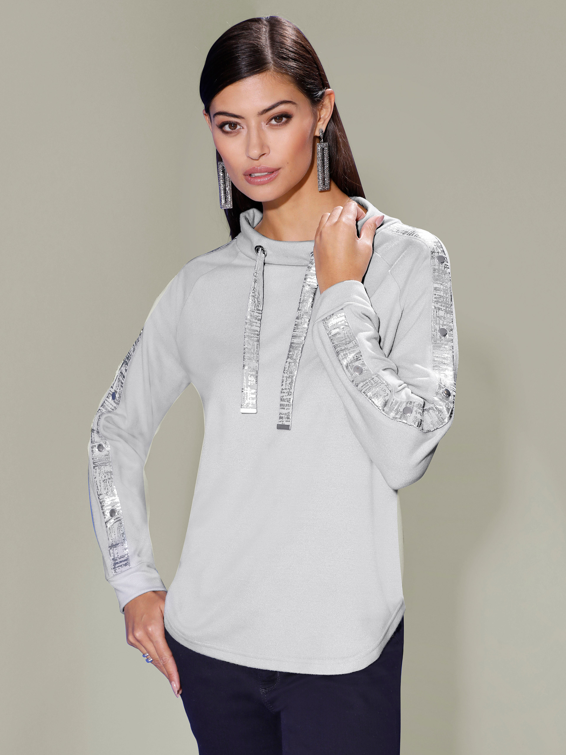 Model mit grauem Pullover steht vor pastellgrünem Hintergrund.