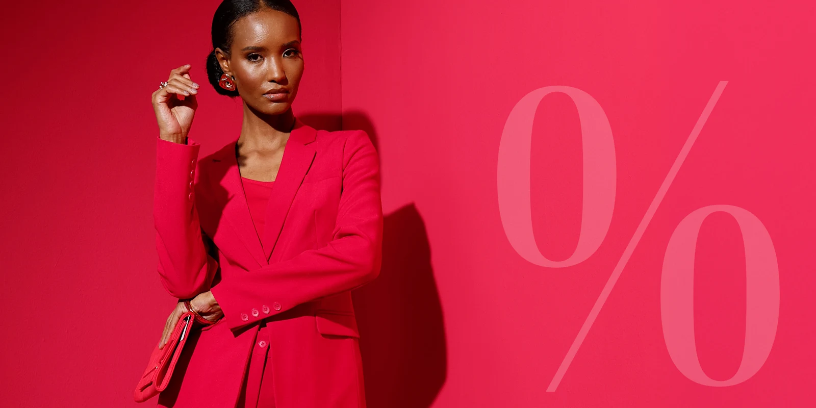 Ein Model sitzt vor rotem Hintergrund, trägt pinkes Jacket und Hose, Hand am Kopf, großer weißer 'Sale'-Schriftzug über dem Bild.