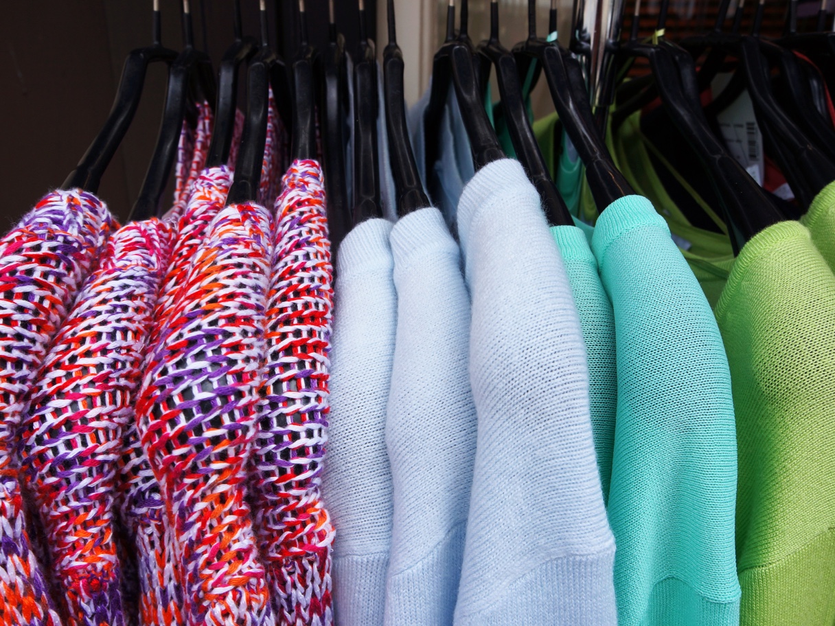 Bunte Strickpullover und einfarbige Pullover in Pastellfarben auf schwarzen Kleiderbügeln.