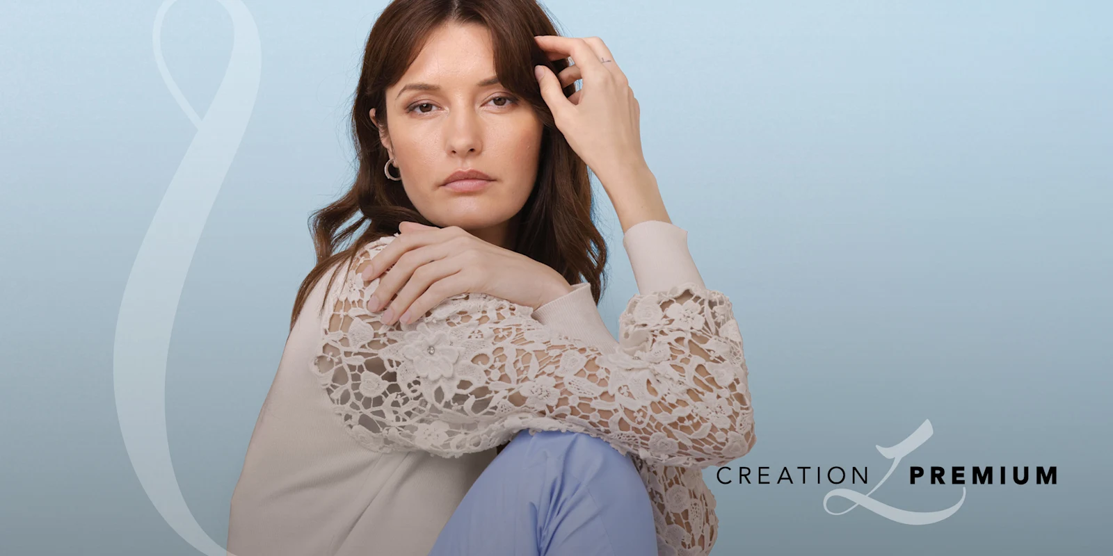 Ein Model sitzt vor hellblauem Hintergrund. Es trägt eine cremefarbene Bluse mit Spitzenärmeln und eine hellblaue Hose. Text: 'CREATION PREMIUM'.