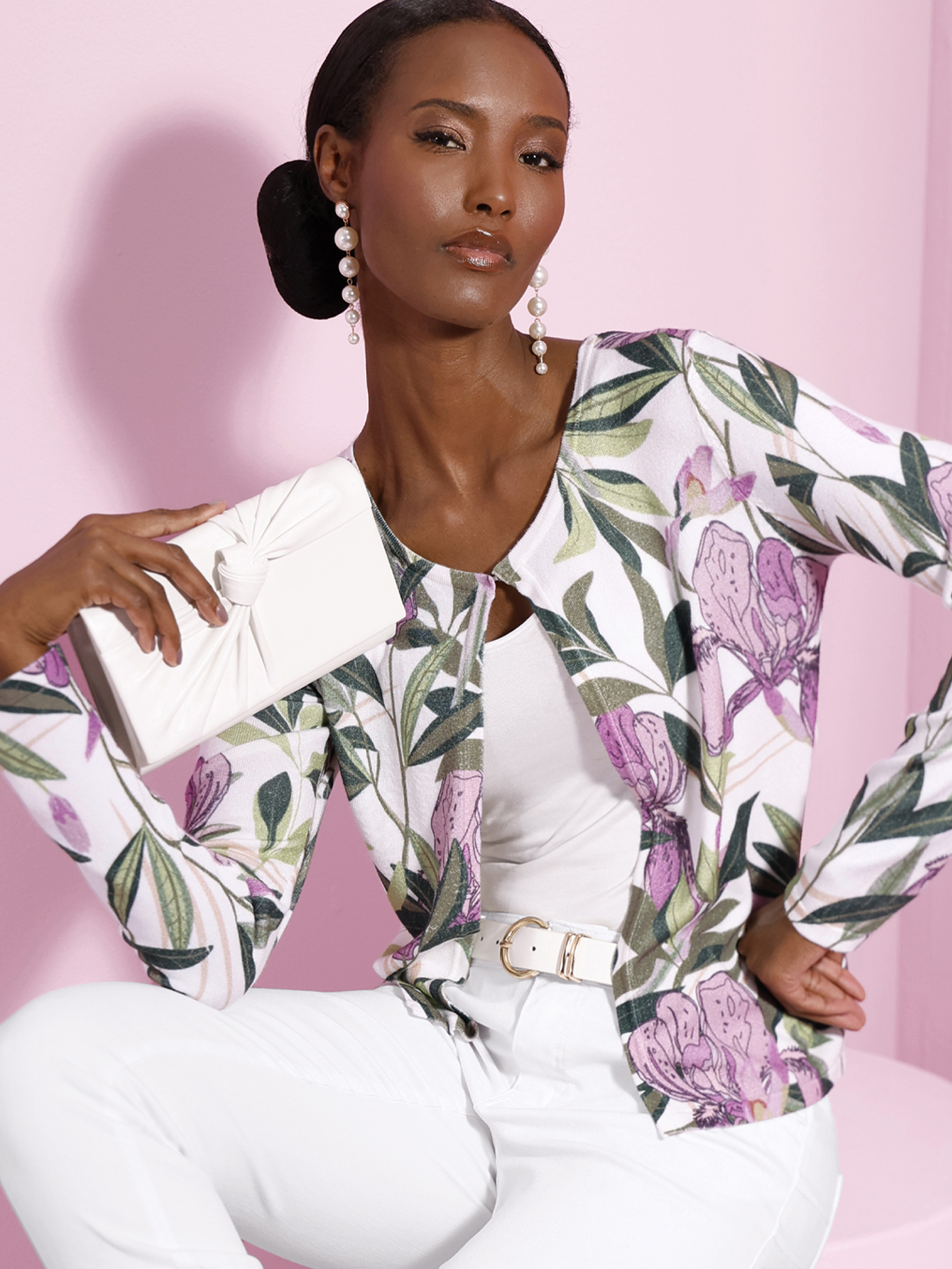 Zwei Models tragen eine weiße Jacke mit lila-grünem Blumenmuster, kombiniert mit weißen Oberteilen vor rosa Hintergrund.