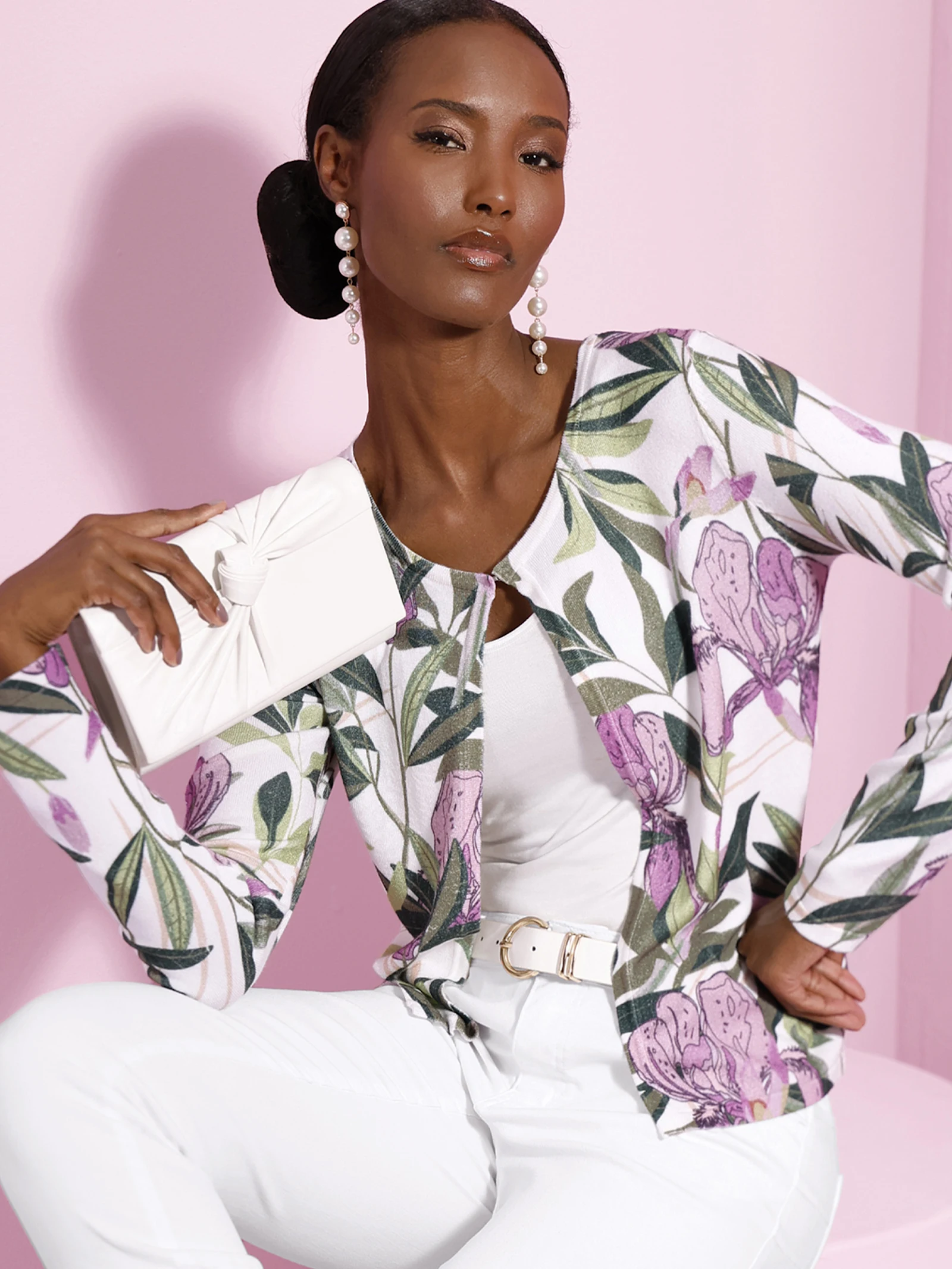 Zwei Models tragen eine weiße Jacke mit lila-grünem Blumenmuster, kombiniert mit weißen Oberteilen vor rosa Hintergrund.