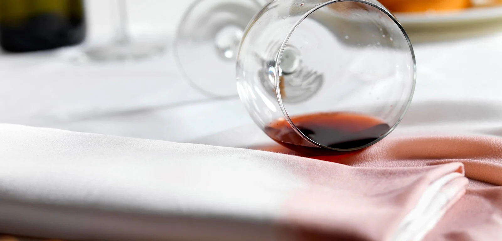 Umgestürztes Weinglas mit Rotwein auf weißer Tischdecke. Umgestürztes Weinglas mit Rotwein auf weißer Tischdecke.