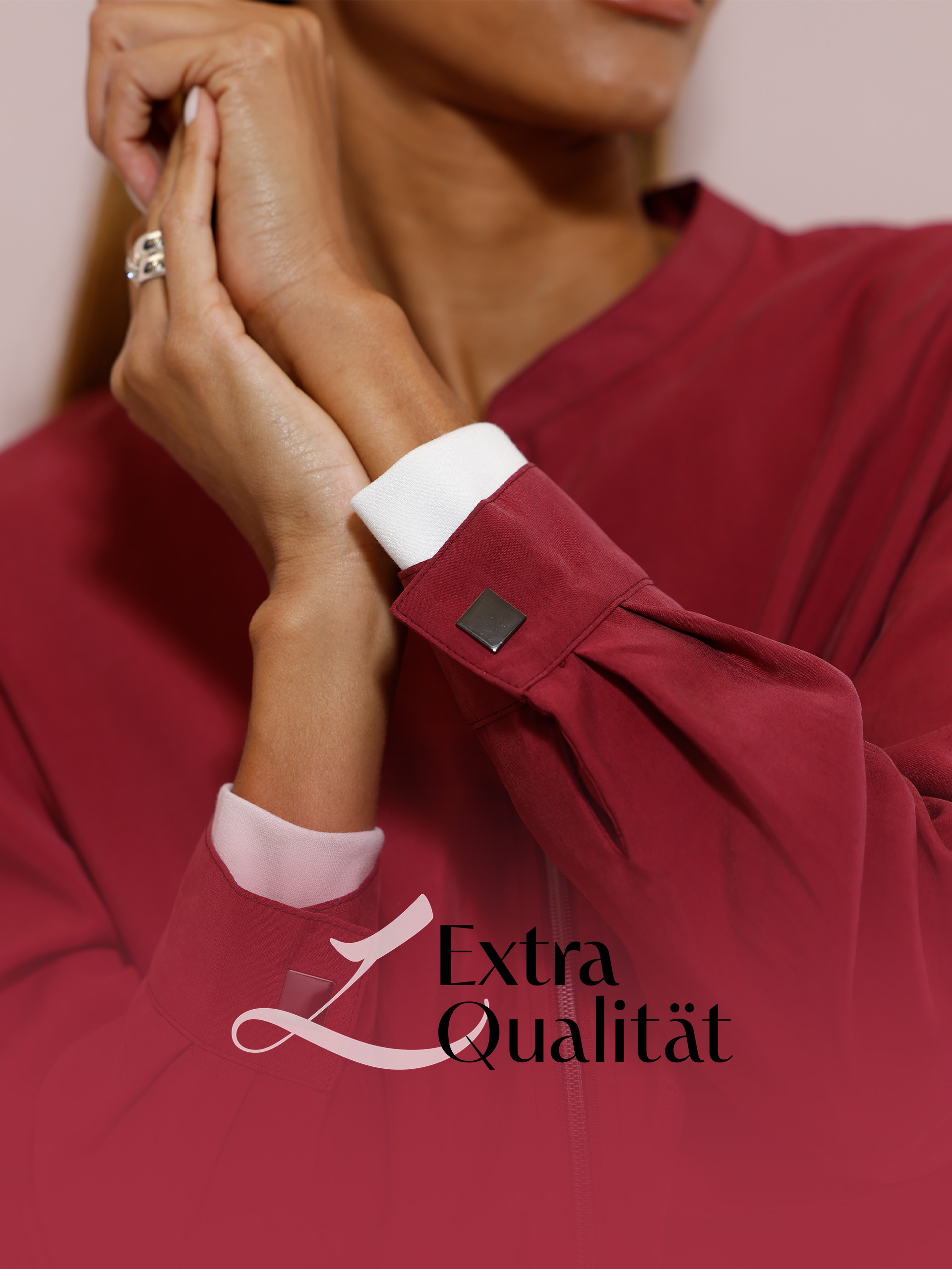 Ein Model trägt eine bordeauxrote Jacke mit weißen Manschetten, der Schriftzug 'Extra Qualität' ist rechts unten zu sehen.