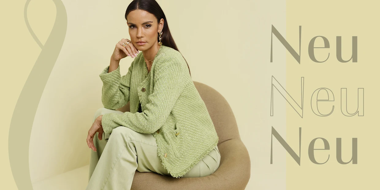 Ein Model sitzt auf einem Stuhl, trägt ein grünes Tweed-Jackett und eine passende Hose.