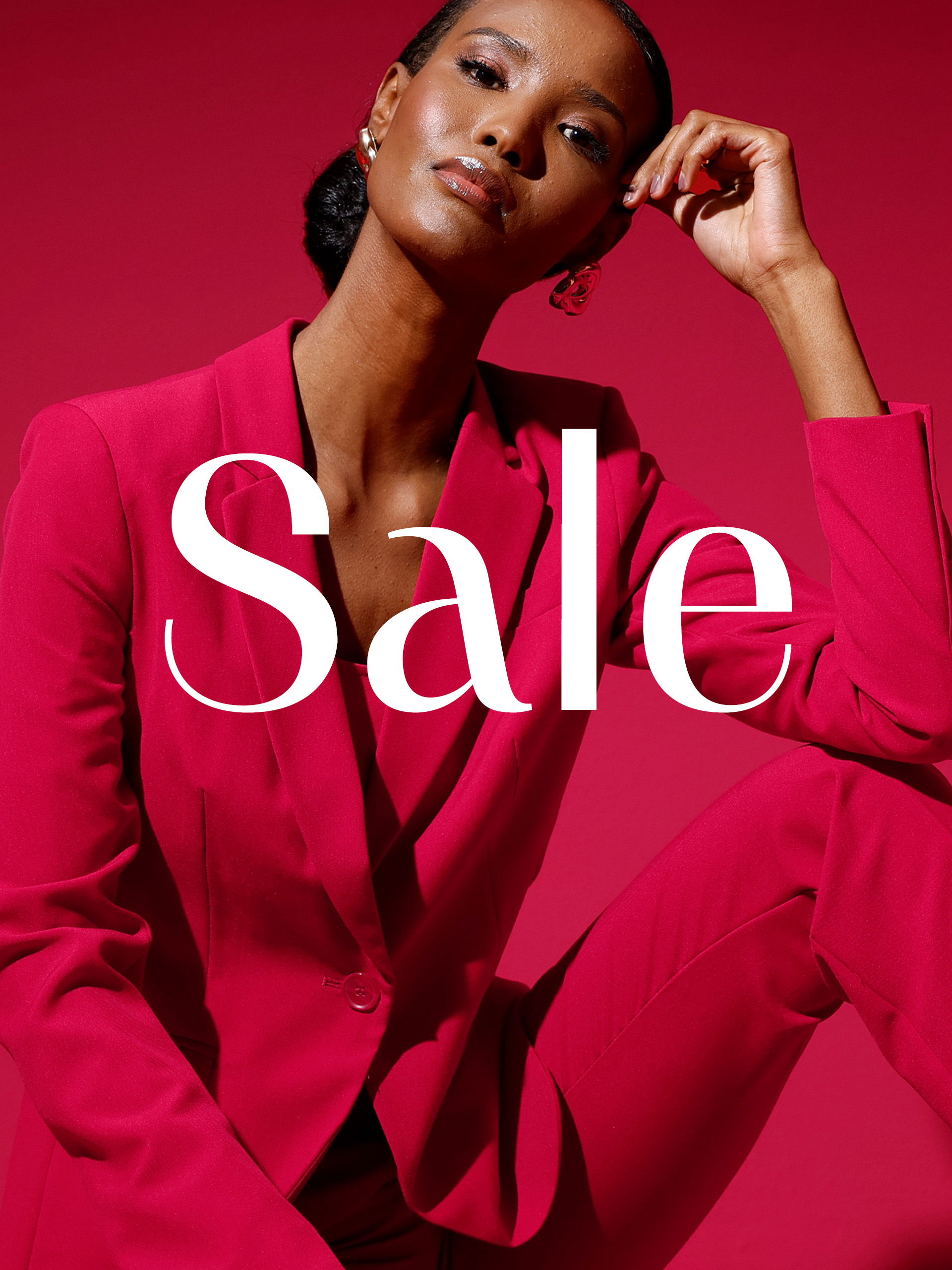 Ein Model im pinken Hosenanzug sitzt vor pinkem Hintergrund, darüber steht groß 'Sale' in weißer Schrift.