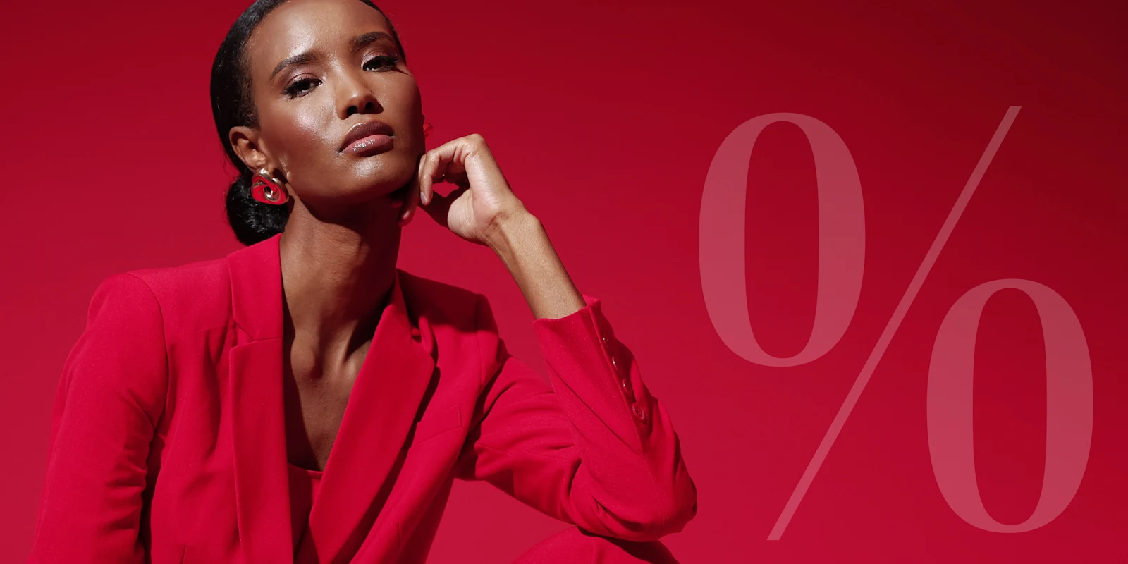 Ein Model sitzt vor rotem Hintergrund in einem roten Anzug, rechts im Bild ein großes, transparentes Prozentzeichen.