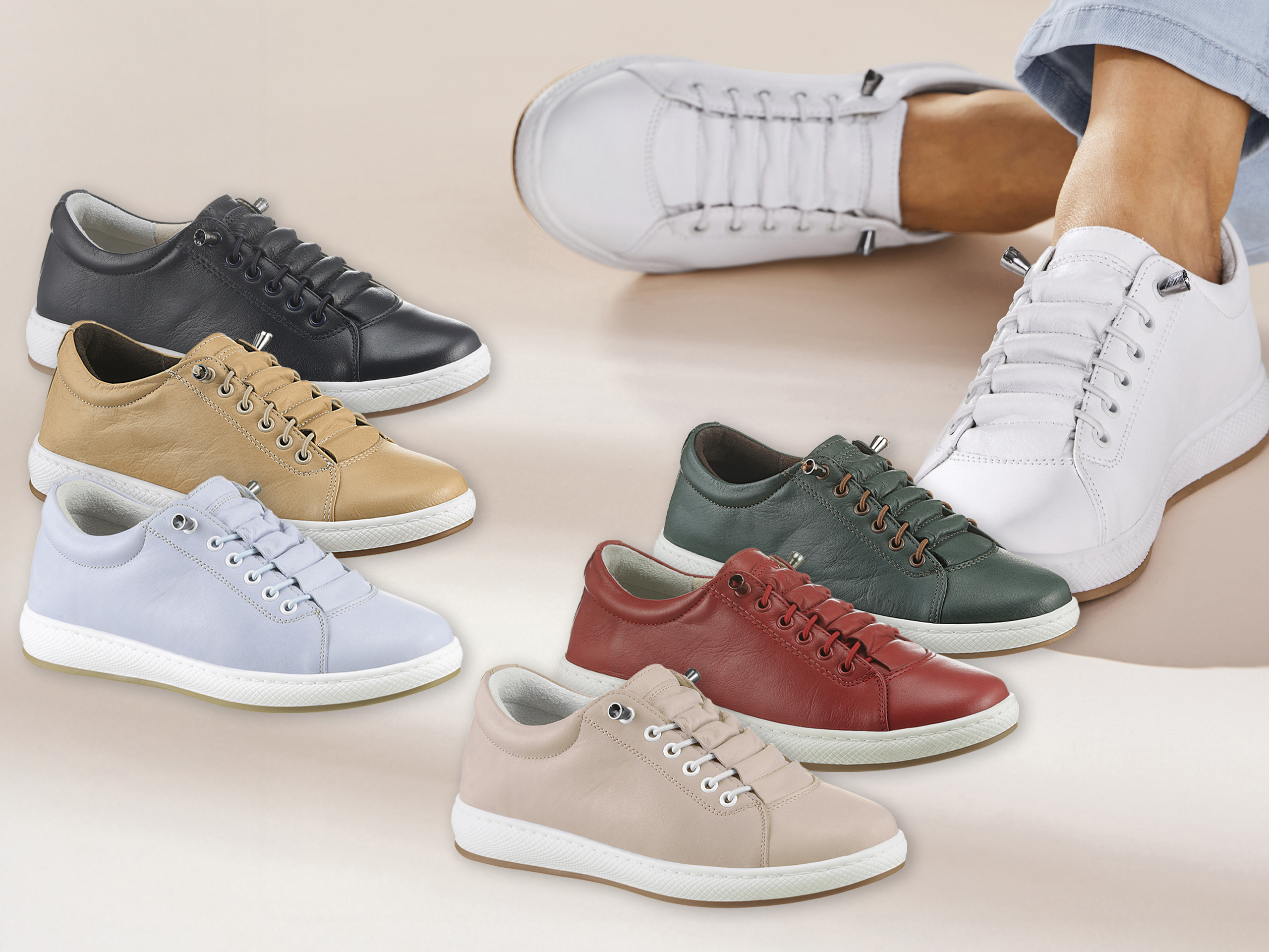 Verschiedene Paar Sneaker aus Leder in sechs Farben liegen nebeneinander, ein Fuß trägt weiße Sneaker.