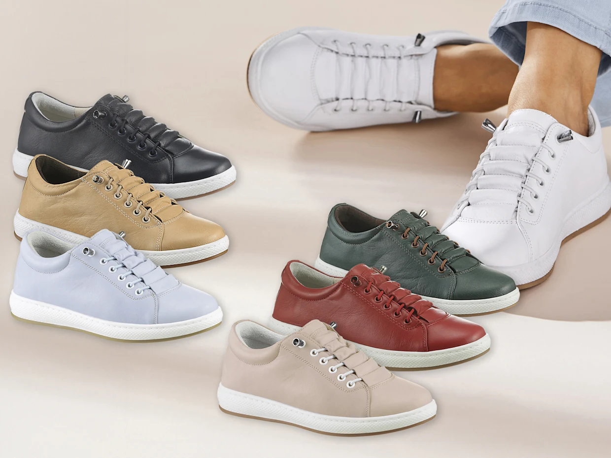 Verschiedene Paar Sneaker aus Leder in sechs Farben liegen nebeneinander, ein Fuß trägt weiße Sneaker.