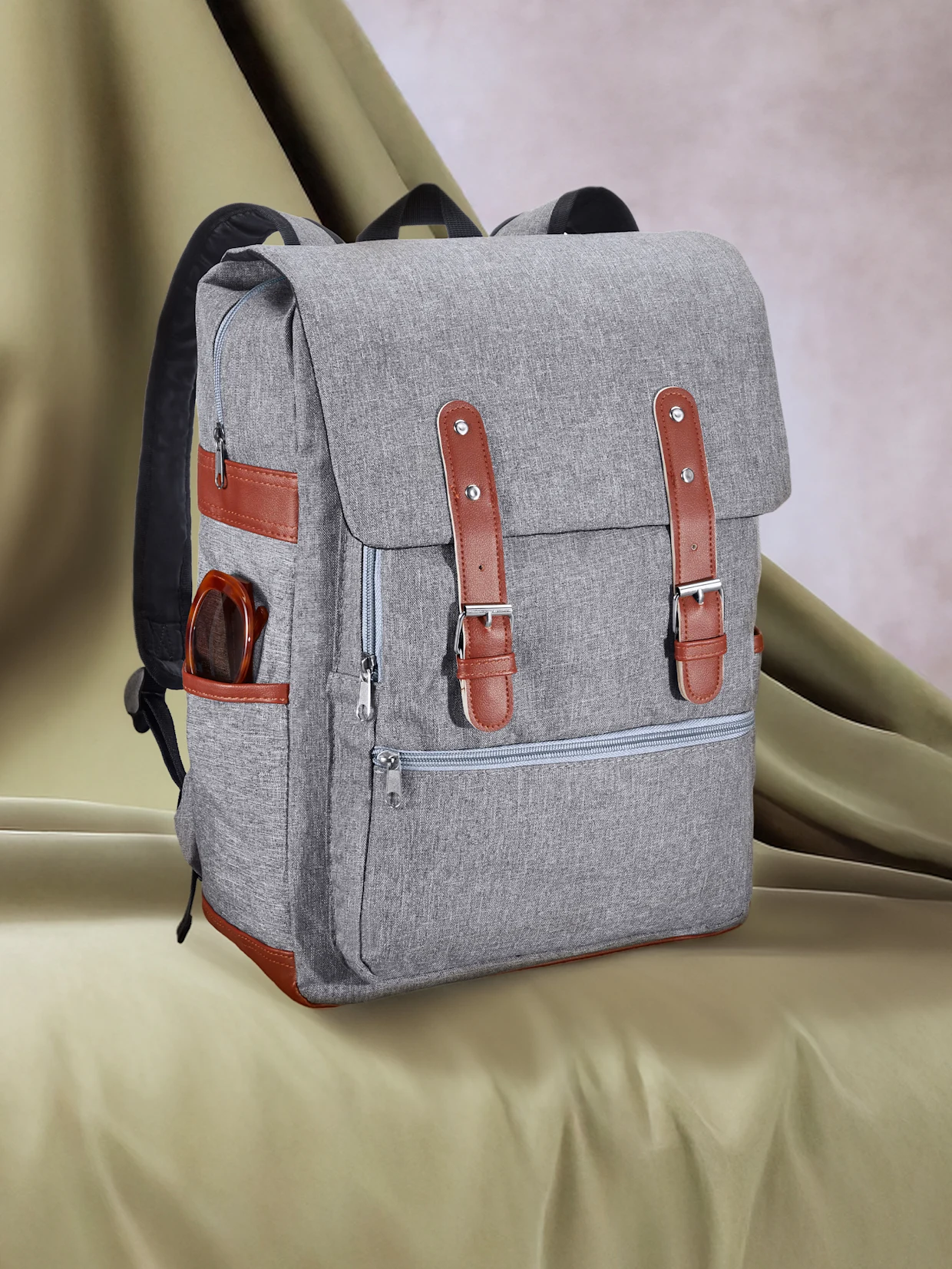 Ein stilvoller grauer Rucksack aus meliertem Stoff, mit braunen Kunstlederdetails und Metallschnallen an der Vorderseite. Eine braune Sonnenbrille steckt in einer Seitentasche. Der Rucksack steht auf einem gerafften, hellgrünen Stoff. Ein stilvoller grauer Rucksack aus meliertem Stoff, mit braunen Kunstlederdetails und Metallschnallen an der Vorderseite. Eine braune Sonnenbrille steckt in einer Seitentasche. Der Rucksack steht auf einem gerafften, hellgrünen Stoff.