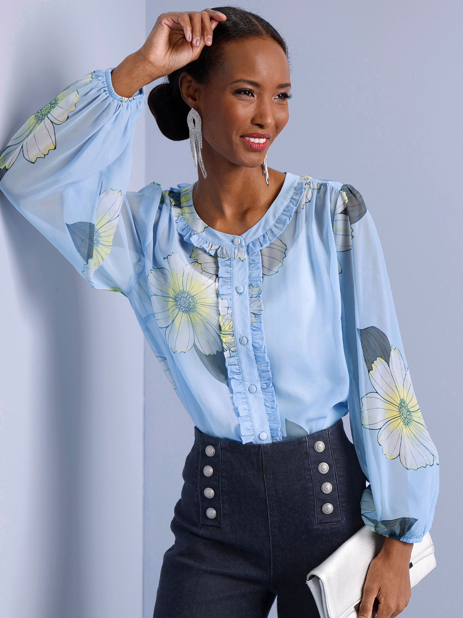 Ein Model trägt eine hellblaue Bluse mit großem Blumenmuster und Rüschenkragen, dazu auffällige Ohrringe. Links steht mehrfach 'Neu'.