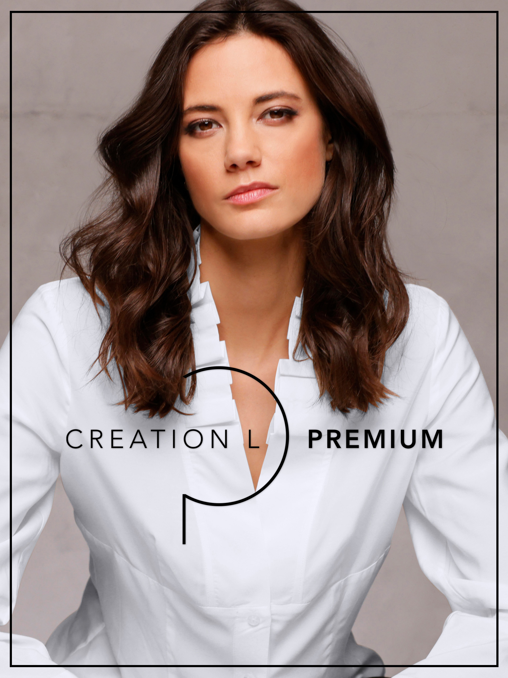Ein Model mit mittellangem, gewelltem Haar trägt eine weiße Bluse vor neutralem Hintergrund. Text: 'CREATION L PREMIUM'.