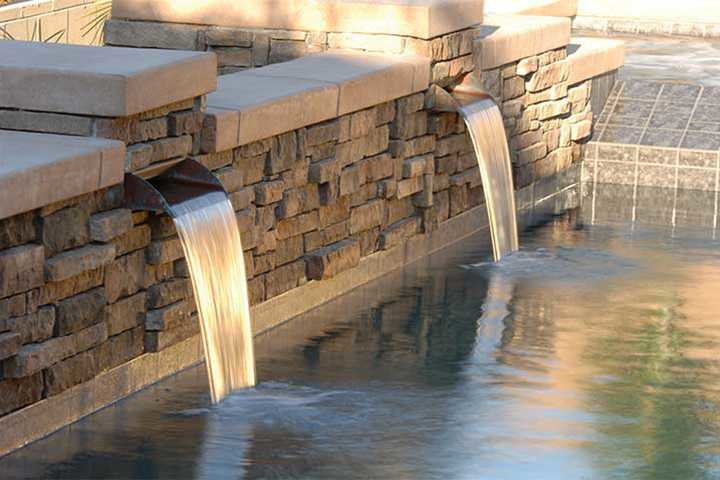 A waterfall is coming out of a stone wall into a pool .