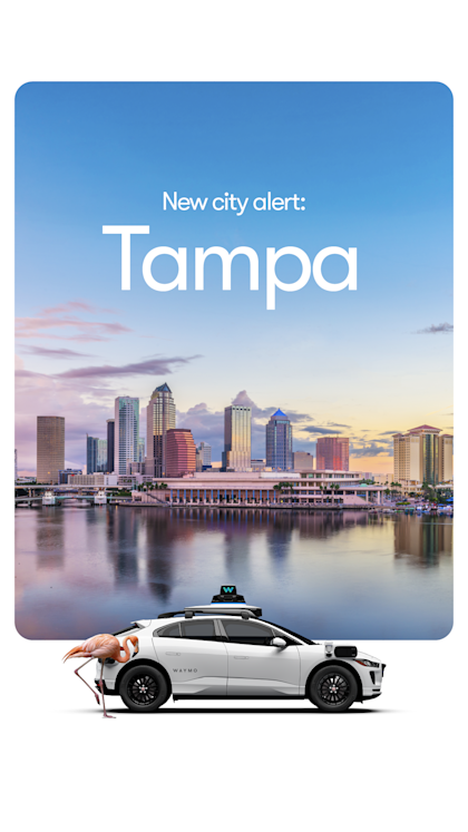 A white, Waymo I-PACE vehicle in front of the Tampa skyline with a Flamingo. 