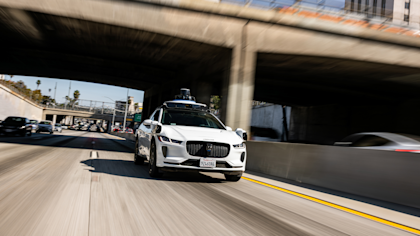 A white, fully autonomous Waymo I-PACE SUV navigating a Los Angeles freeway.